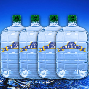 Four large plastic jugs of Crystal Premium Spring Water with green caps are lined up in front of a blue background with water at the bottom, making them a perfect addition to any Bottle Plan or 3 Gallon Glass set-up.